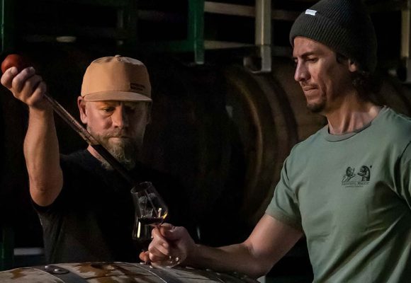 men in barrel room extracting beer from barrel